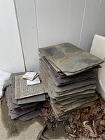Photo of stacked rectangular slate sheets with smaller tiles on top outdoors on concrete and leaf debris visible.
