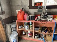 Wide view of shelving unit with various paint cans, gas cans, and other items on and around it
