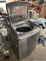 View from top showing the open lid revealing the drum interior. The machine is metallic grey with a transparent window on the lid.