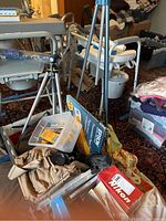 Two aluminum tripods standing behind tan canvas bag holding Nikon camera, Nikon lens cap, Kodak film and other accessories