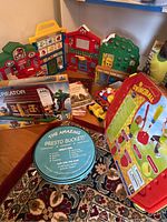 Photo showing multiple items including Fisher-Price Little People activity center, children's books, swing ball game, LEGO set box, and Presto Bucket on carpet