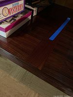 Top-down view of table surface showing wood grain pattern and inset border detail, game boxes on top for scale.