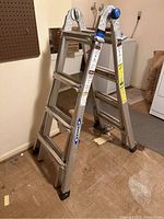 Full view of the aluminum multi-position Werner ladder standing open in a room, showing metal frame and steps.