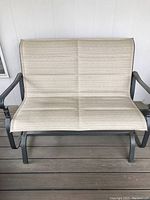 Front view of Hampton Bay glider bench showing beige fabric seating and backrest with metal armrests.