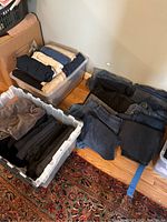 Multiple pairs of women's jeans and pants folded and stored in clear plastic bins and laid on the floor, showing variety of colors and fabrics.