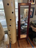 Wooden jewelry armoire standing next to round plastic storage tower in room setting