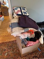 Stack of assorted blankets, quilts, and other linens in a large cardboard box