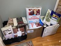 Wide view of entire lot showing packed sheet sets, pillows, blanket, and hangers arranged on floor against wall.