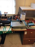 Wide shot of office desk with organized office supplies including pens, knife kit, paper trimmer, keyboard box, coloring books