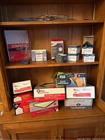 Office supplies arranged on wooden shelves, showing writing pads, postage labels, envelopes, plastic bindings.