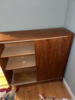 Front view of wooden sliding door cabinet with door partially open revealing interior shelves and wood grain.