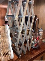 Wooden folding wine bottle storage rack with brass fasteners and part of the other items behind it on a wooden table