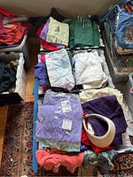 Photo showing multiple stacks of folded women's clothing including sweatshirts, tops, and sweaters in various colors and styles.