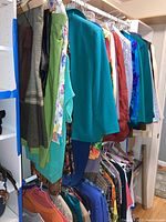 Two racks of women's clothes including skirts, tops, jackets, sweaters, and pants in various colors and fabrics.