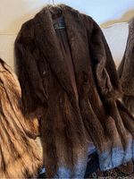 Front view of dark brown fur coat draped over sofa showing overall appearance and length.