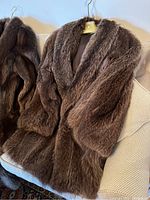 Full front view of brown fur coat hanging on Garfinckels hanger over chair