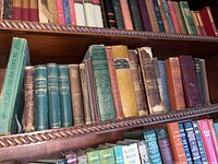 Antique bookshelf showing a variety of classic and antique books in worn condition, including poetry and historical titles.