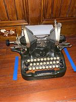 Image of the full typewriter showing metal green base, double curved type arms, and full set of cream colored keys.