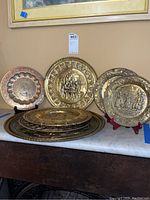 Group of decorative brass-tone metal plates with repoussé designs in various sizes on a marble surface.