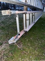 Full side view of extended ladder showing aluminum rungs and fiberglass rails with rubber-tipped feet on grass.
