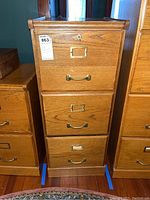 Front view of the wooden file cabinet showing three drawers with metal handles and label holders, keyhole on top drawer, worn finish.