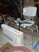 Photo showing bath/shower sliding chair with metal frame, white plastic perforated seat and backrest, black safety strap, and original iWalkFree crutch box underneath.