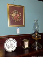 Overview of the lot showing the framed embroidered floral artwork, small clock, display plate and glass oil lamp.