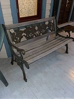 Bench viewed front and side showing wooden slats and cast iron floral decorative back and armrest.
