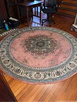 Full view of the round Oriental style rug placed on a hardwood floor, showing pink background and central medallion design.