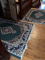 Two matching area rugs laid on hardwood floor near staircase, showing overall size and placement.