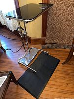 Photo showing the black glossy adjustable standing desk on chrome frame with wheels and anti-fatigue mat beneath.