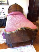 Full view of the vintage twin sleigh bed with pink bedding in a room with wooden floors and antique style decor.