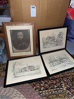 Framed portrait and three framed architectural sketches of Williamsburg buildings placed on floor next to large cardboard box