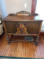 Front full view of the vintage wooden bar cabinet showing carved front doors and raised back ornament.
