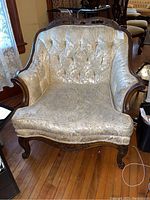 Front view of the vintage chair showing tufted damask upholstery, wooden frame, and curved armrests.
