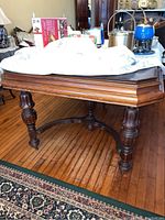 Photo of vintage wooden dining table with carved legs and ornate stretcher on hardwood floor, covered partially by cloth and items.