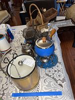 Photo showing vintage kitchen tools including blue fondue pot on stand with burner, metal ice bucket, tea pot, and various other vintage kitchen accessories on a table with lace tablecloth.