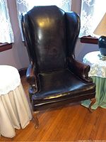 Front view of the vintage wingback chair showing dark brown leather, winged high back, and curved armrests.