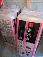 Four unopened bags of pink fiberglass insulation stacked in a utility area