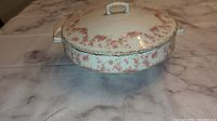 Side view of covered china dish showing decorative floral pattern and gold trim on base and handles.