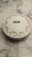 Top view of the round covered dish showing pink rose garland on lid and white porcelain with handles.