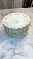 Stack of 12 large shallow bowls showing the gold-trimmed scalloped edges and floral decorations.