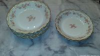 Stack of 6 medium shallow bowls and 2 small shallow bowls arranged on fabric background showing floral pattern and gold trim.