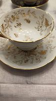 Tea cup and saucer set with intricate gold floral pattern and gilt rims on white bone china.
