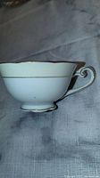 Side view of the white porcelain tea cup with gold trim and handle detail.