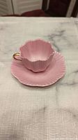 Pink tea cup with scalloped rim and matching saucer on white cloth