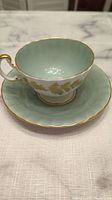 Tea cup and saucer side view showing mint green interior and gold leaf decoration with gold rims.