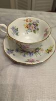 Bone china tea cup and saucer with floral design and gold trim on a white fabric background.