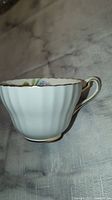 Side view of the Paragon fine bone china tea cup showing the white ribbed texture and gold rim.