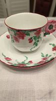 Handcrafted tea cup on matching saucer showing pink floral pattern and scalloped edges with flower-shaped handle on cup